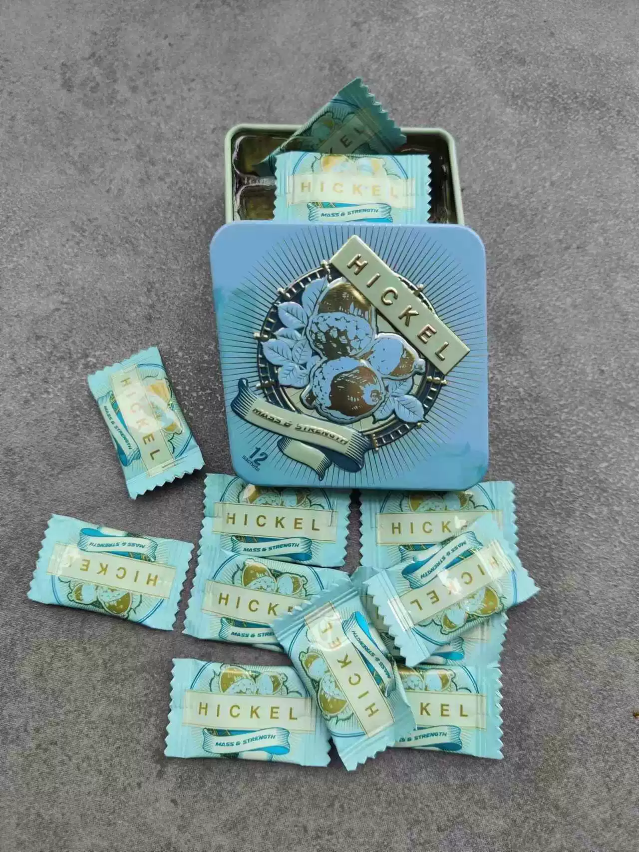Open blue HICKEL tin with individually wrapped bars on a grey surface