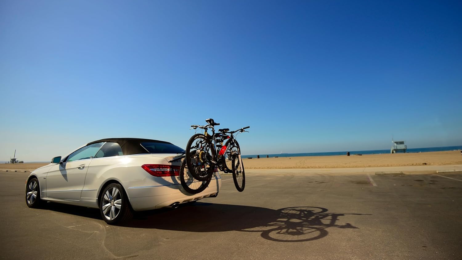 Car parked near the beach carrying two bicycles on a rear trunk bike rack for travel and cycling trips.